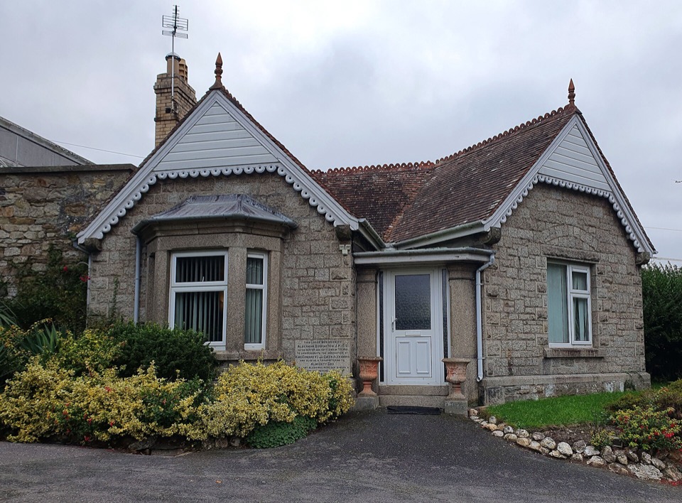 A granite lodge with a lawn and a gravel drive at Victoria Gardens in Truro, Cornwall